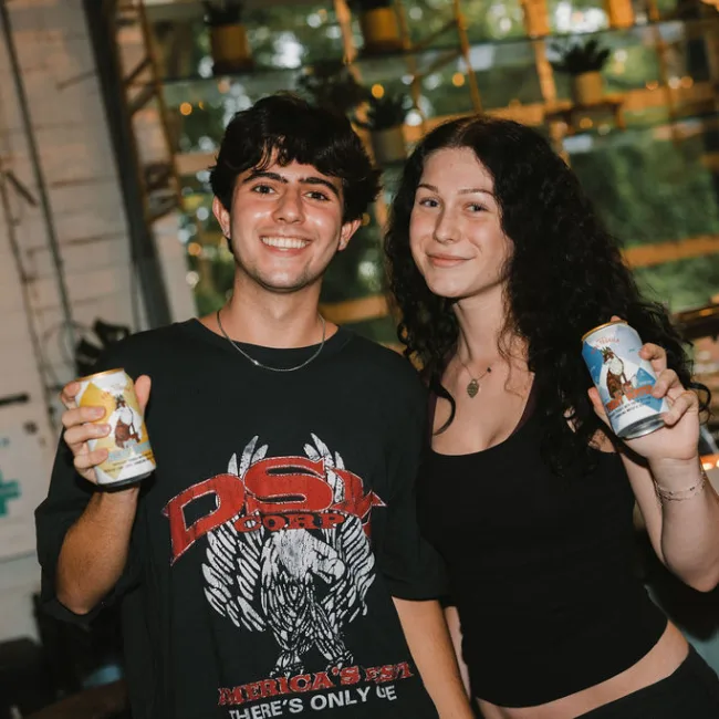 Guests holding cans of Yacht Water at the Yacht Club happy hour